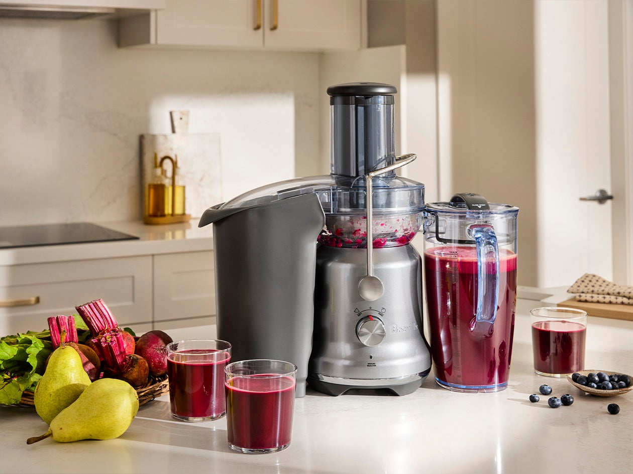 Freshly made juice displayed alongside a juicer, fruits, and vegetables in a bright kitchen.