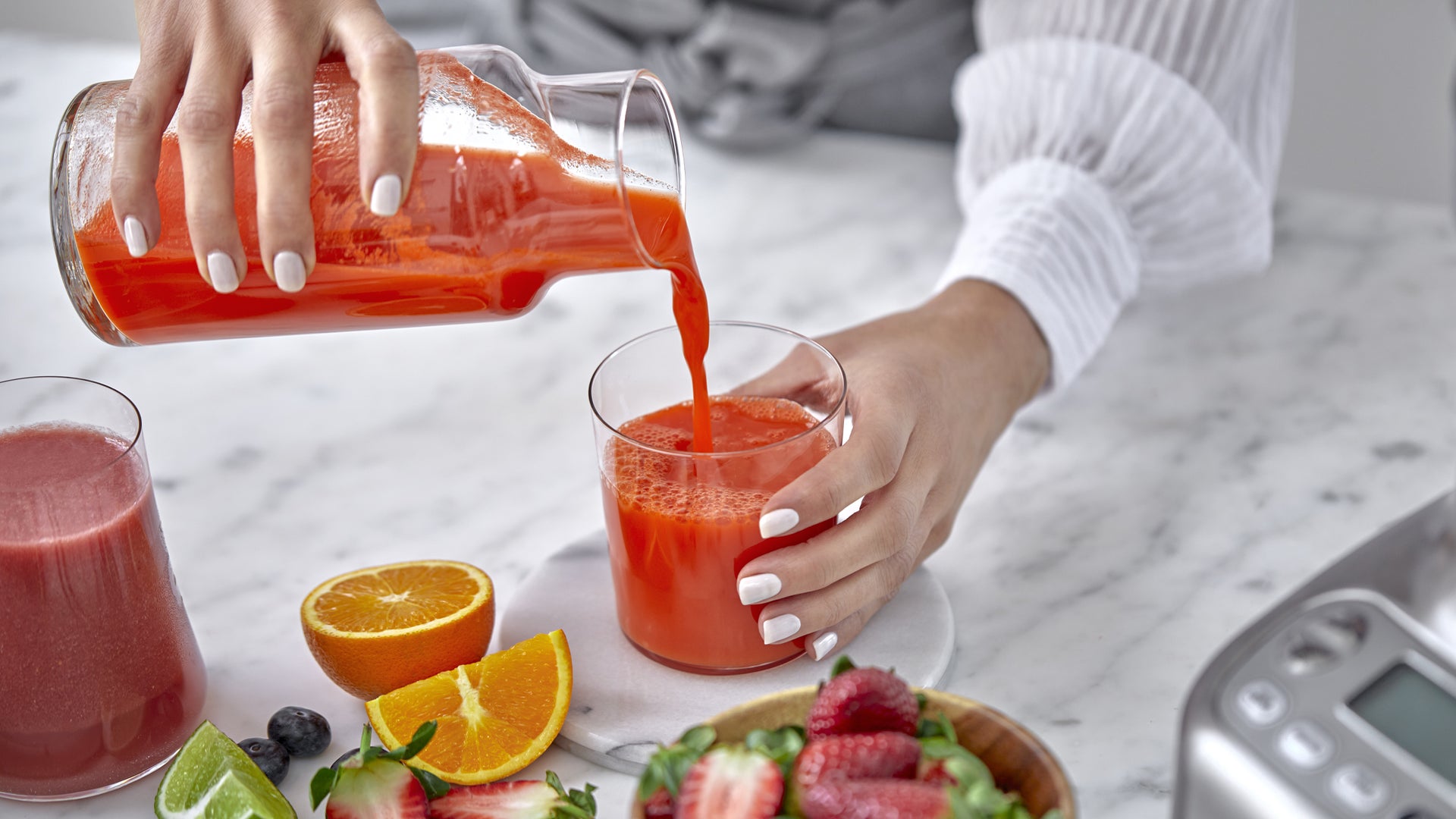 Fresh juice being poured into a glass with fruit nearby.