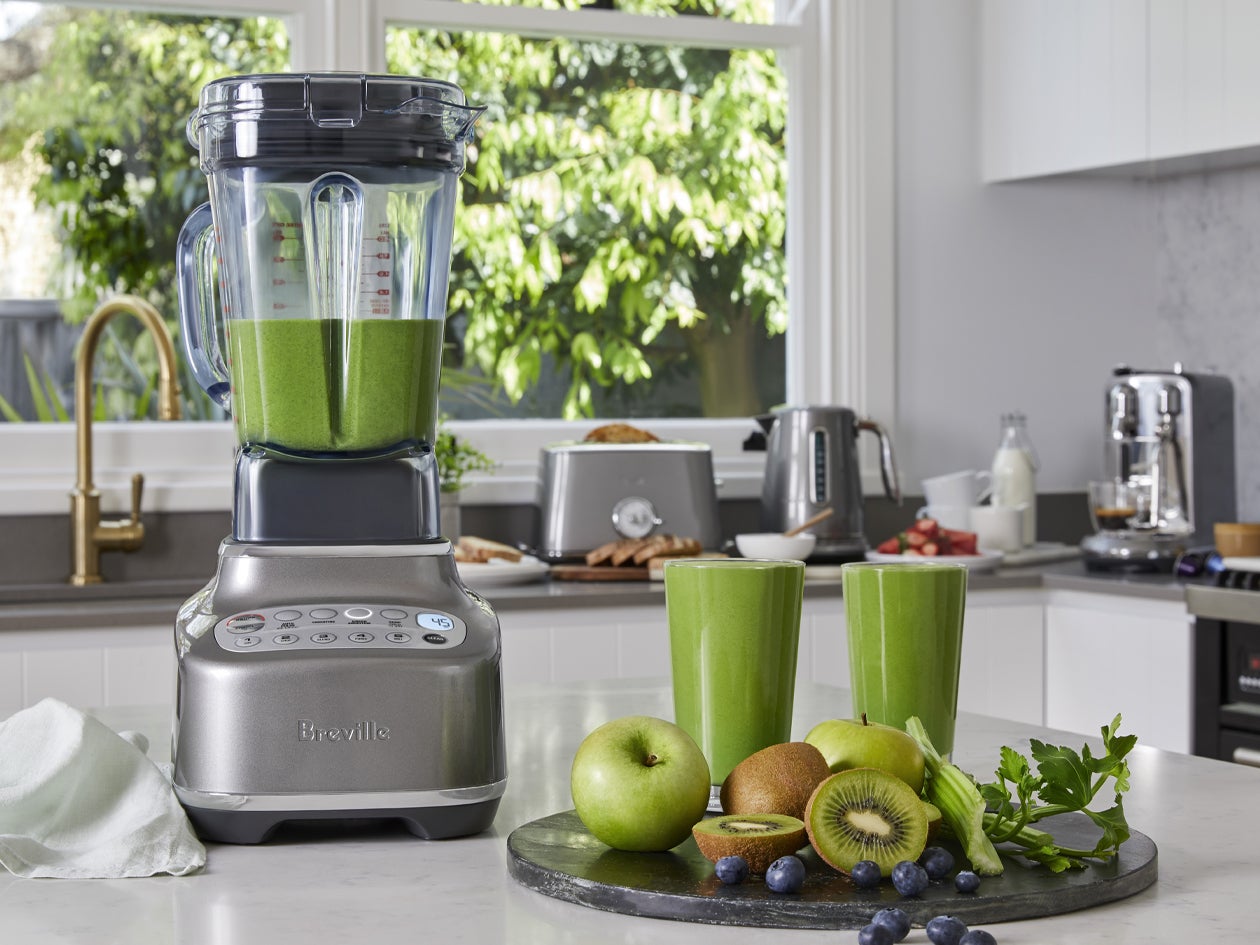 Blender shown with green smoothies, fresh fruit, and vegetables.