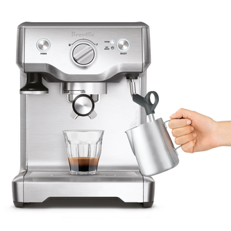 Front view of someone using the steam wand and a glass of coffee sitting on the Duo-Temp Pro.