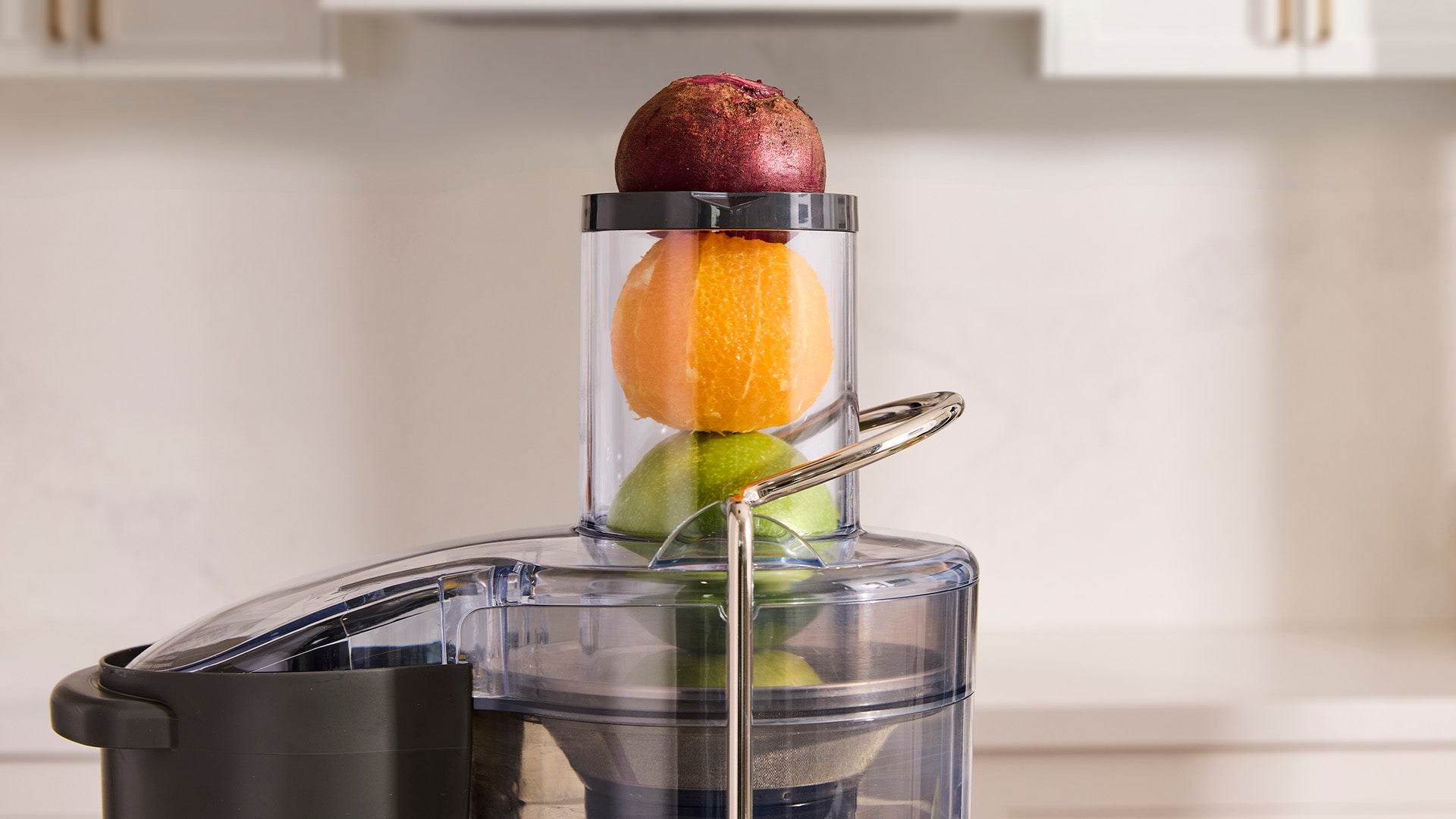 Close-up of a juicer with whole beetroot, orange and lime stacked in the wide feed chute, ready for juicing.