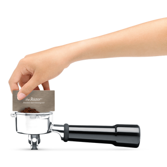 Someone using the Razor precision tool to remove excess ground coffee from the portafilter.