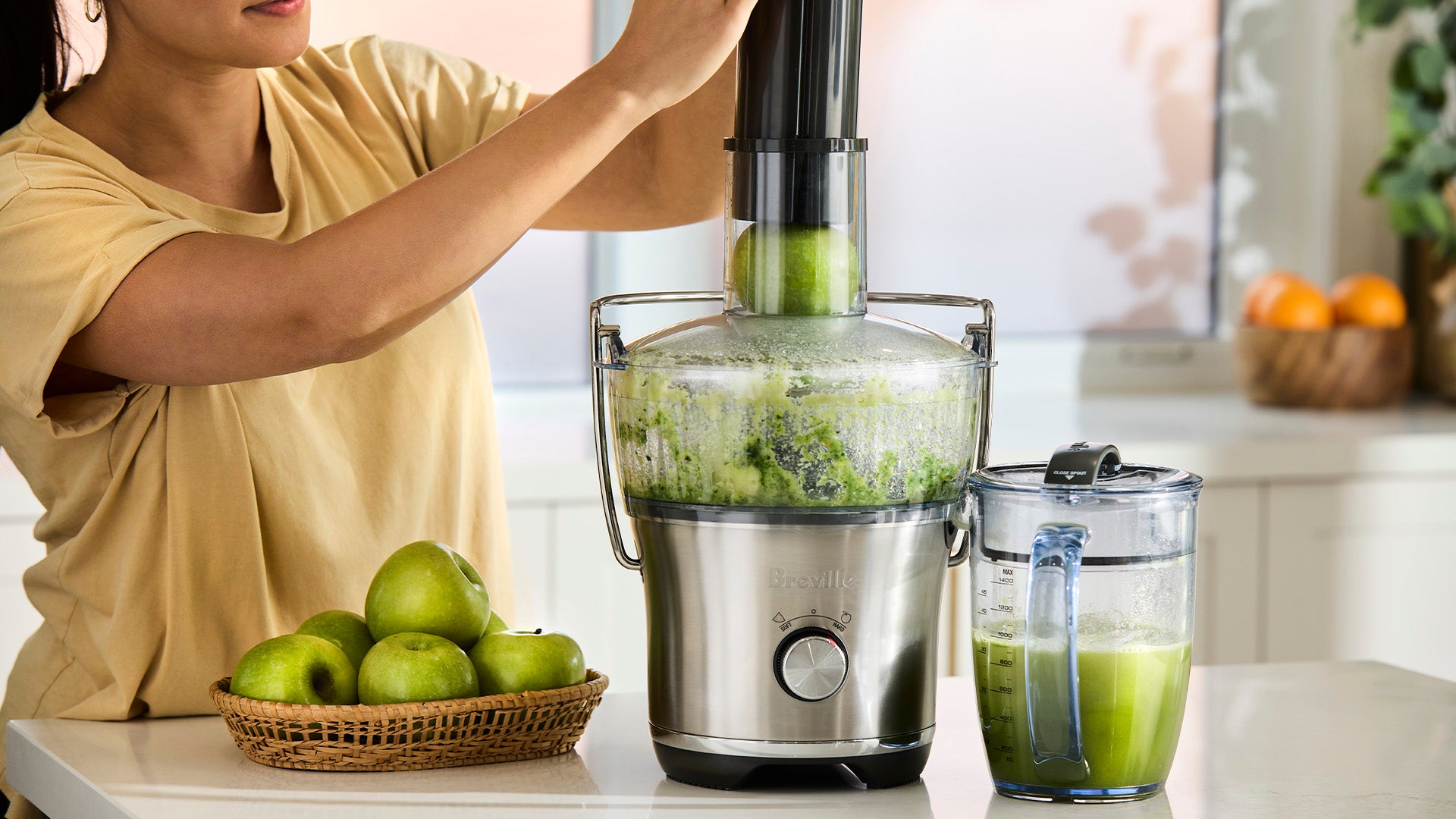 Person using a juicer to make fresh green apple juice, with apples in a basket beside the machine.